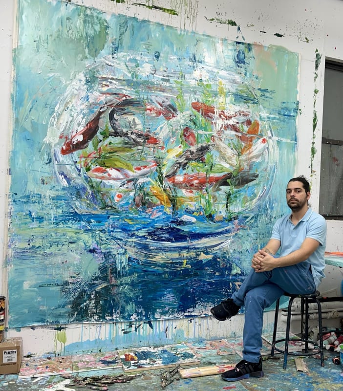 Cuban Artist, Eric Alfaro, sits in front of one of his renowned fishbowl paintings. Presented by Carousel Fine Art, Alfaro's "Aquarium" series redefines the essence of traditional Still Life paintings.
