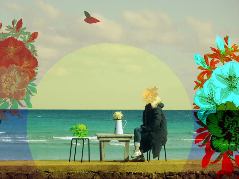 women on beach with coat on and flower over her head and other flowers