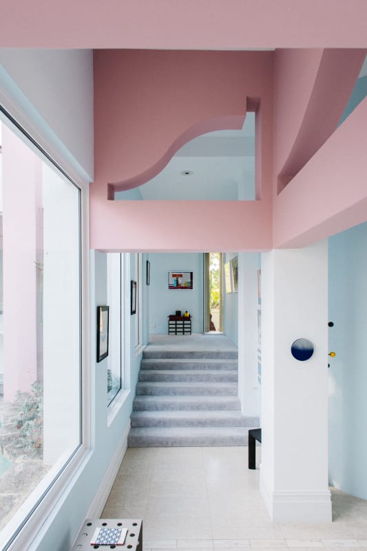 Interior view of OFFMARKET Gallery showing a light-filled corridor with pastel pink and blue architectural details, large windows, and framed artworks along the walls.