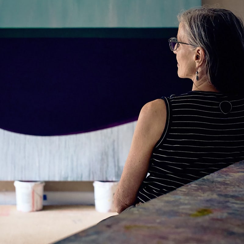 Photograph of artist Sarah Hinckley at her Cape Cod painting studio, sitting with one of her large oil on canvases.