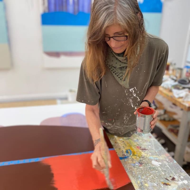 Sarah Hinckley at work on a large painting in her studio, applying bright red paint to a color field.