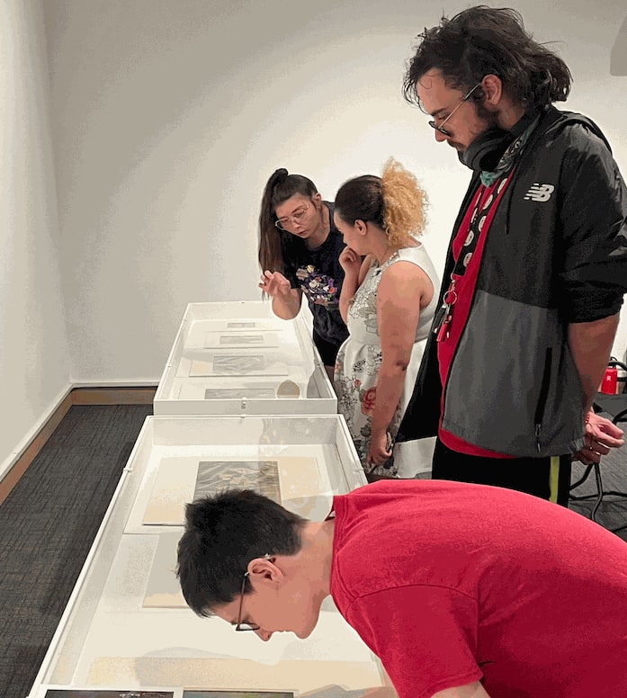 Four students bend over to look at Disney cel paintings in a display case