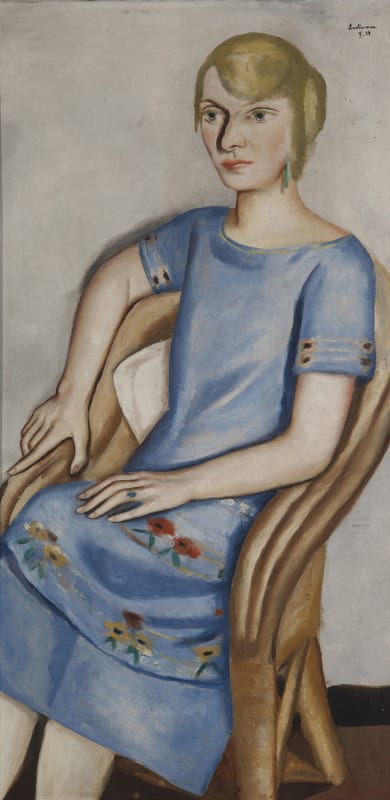 a life-sized, long vertical portrait by Max Beckmann showing a blond white woman sitting in a chair. The space she occupies is shallow with a gray background. She wears a medium blue dress with floral trim details. With a stern expression she looks off to