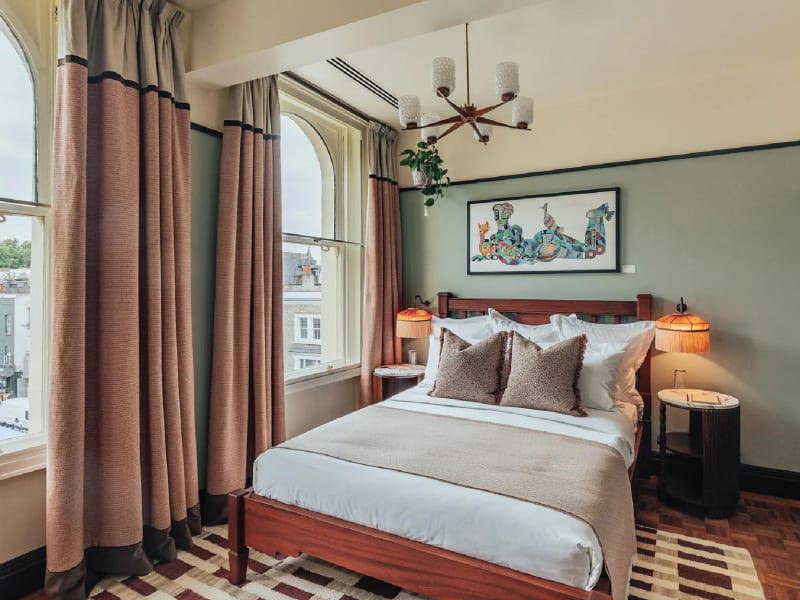 The second bedroom at ‘Permit Room Lodgings’ is a visual delight—anchored by tasselled lamps, Tarini Sethi’s evocative artwork ‘Monday Malaise’ and a window that frames the storied ‘Electric Cinema’ of Notting Hill. Image Credit: (Permit Room Lodgings)