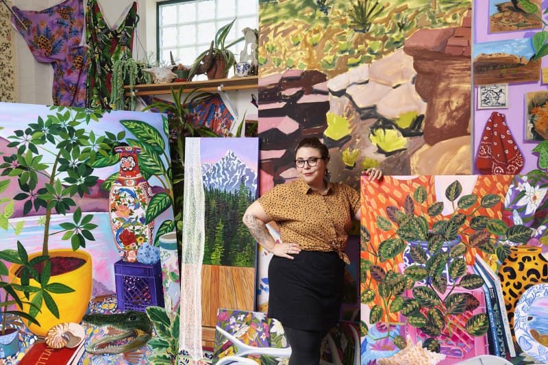 Portrait of Anna Valdez in her studio, standing among her large, vibrant paintings.
