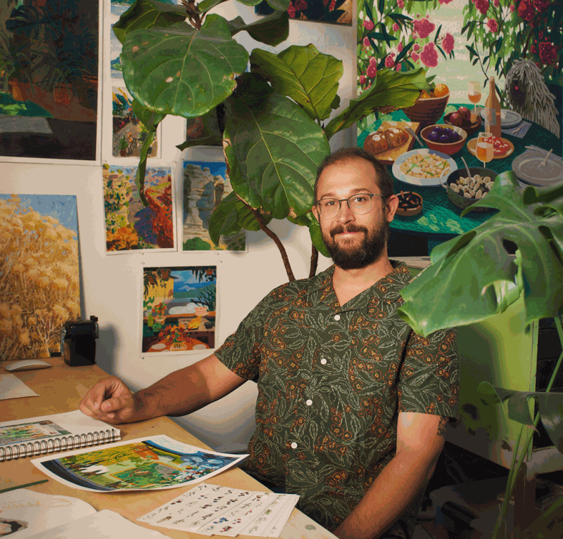 Artist Nicholas Bono Kennedy sitting in his studio surrounded by his paintings