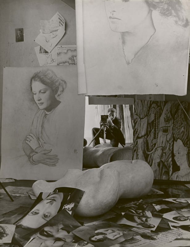 Erwin Blumenfeld self portrait in mirror with women's portraits strewn about studio