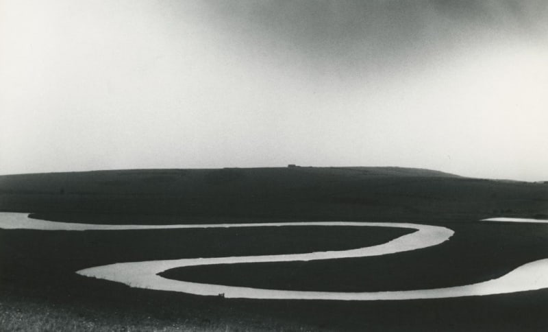 Bill Brandt photograph in black and white of winding Cuckmere River against dark landscape and gray sky