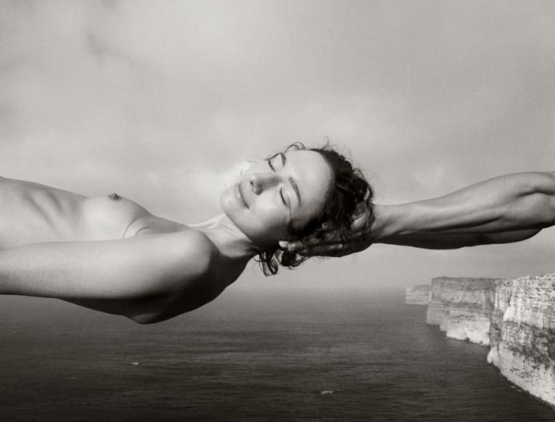 Arno Minkkinen hands outstretched over ocean with nude woman seemingly levitating over the water with her eyes closed