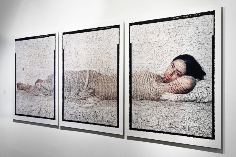 Installation view of triptych of woman reclining in Odalisque pose, her body inscribed in calligraphy made from henna, by Lalla Essaydi