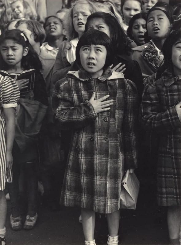 Japanese American schoolgirl amongst classmates of different races saying the pledge of allegiance with her hand on her chest