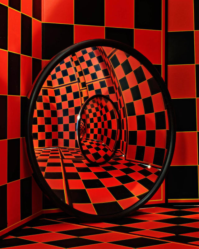 two round mirrors in a red and black checked room reflecting a maze of red and black checked rooms