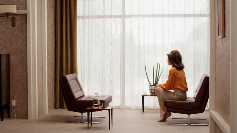 woman in orange shirt sitting in chair looking toward a window with the curtain drawn, by Erwin Olaf
