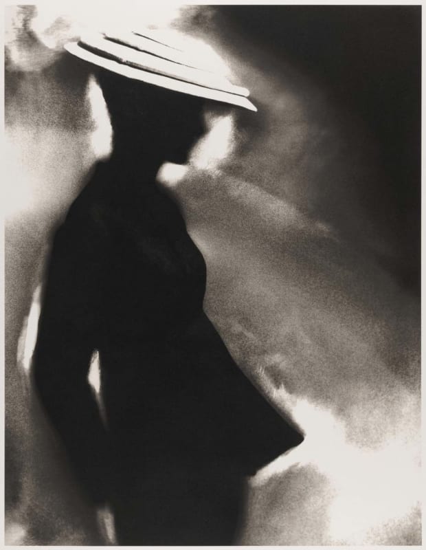 Black-and-white photograph by Lillian Bassman showing a silhouetted figure in a brimmed hat, rendered in soft focus with glowing highlights and abstract form.
