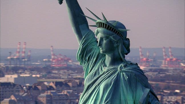 A closeup of the Statue of Liberty against the city.