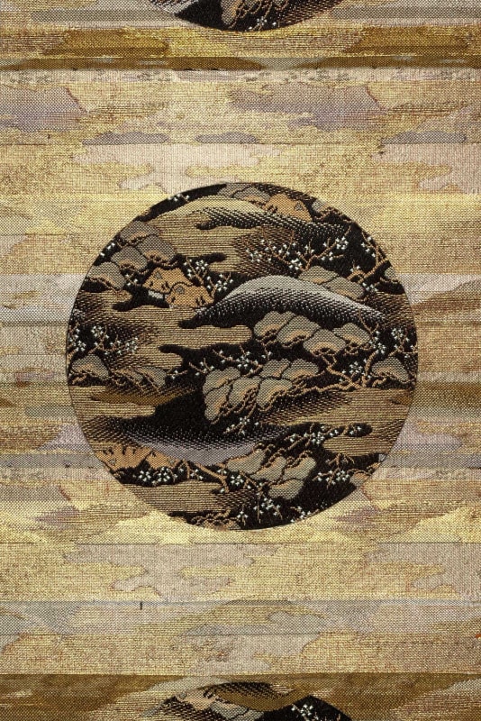 A detail of a gold Japanese scroll; the inlay is a circle in black with a backdrop of a mountain surrounded by gingko-like leaves.