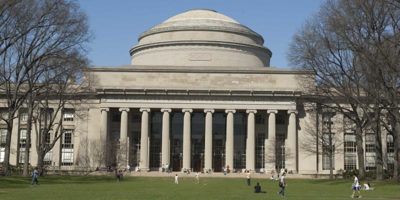 Landscape image of a building with many columns and a dome. In front, people lounge on a lawn.