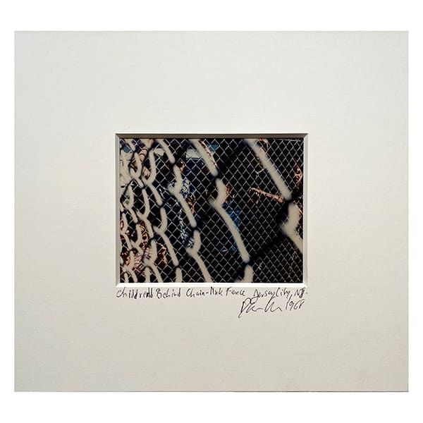 A matted photograph of children behind a chain-link fence