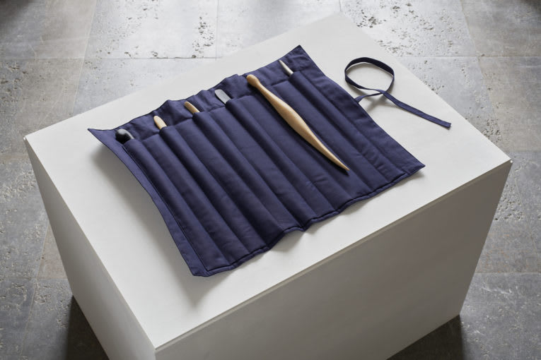 Carving tools in a blue fabric case on a white pedestal