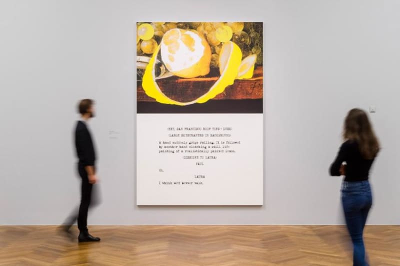 Installation image. People admire piece depicting unraveling lemon on the top and text on the bottom.