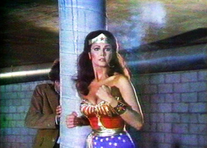 A grainy image of Wonder Woman standing in front of a pillar and a man.