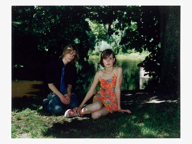 photographic portrait of two people lounging under a tree by stream