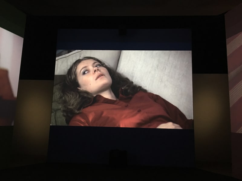 Video still, person lying on couch in red shirt glancing to their right.