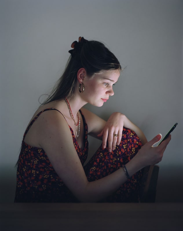 photograph of artwork by Rineke Dijkstra, called Julia, Amsterdam, March 7, 2022, from 2022; Julia is seen staring into a smartphone