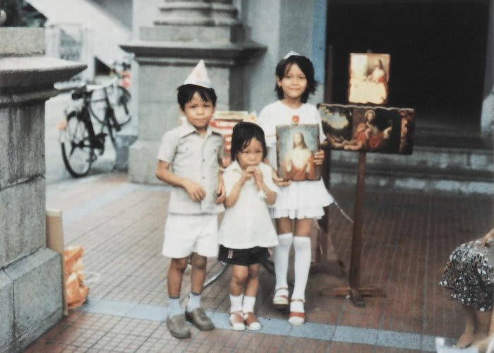 Vintage image of a three children posing for the camera holding Catholic memorabilia.