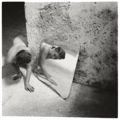 Black and white image of a person crawling around a corner. They encounter a mirror.