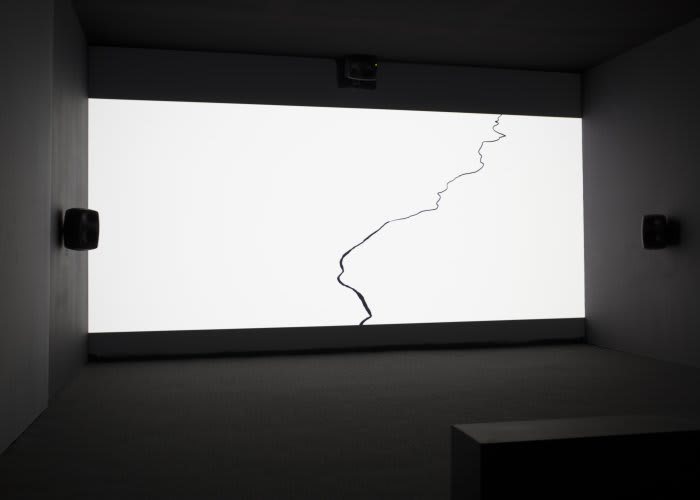 A dark room is illuminated by a white screen with a sinuous black line.