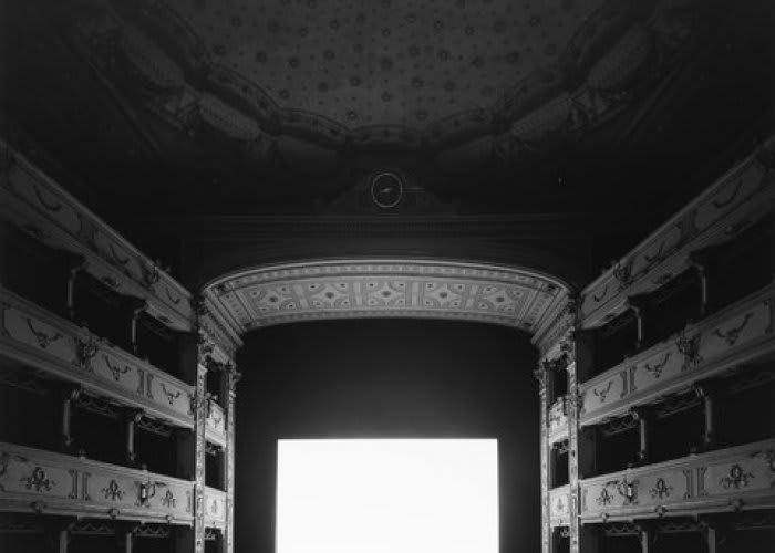 Black and white image of the interior of a decorative auditorium with an illuminated movie screen.