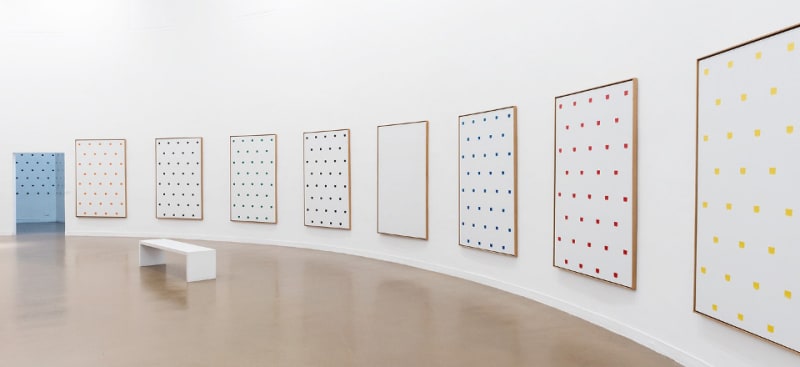 Gallery view of eight large Niele Toroni paintings featuring equidistant square brushstrokes of different colors.