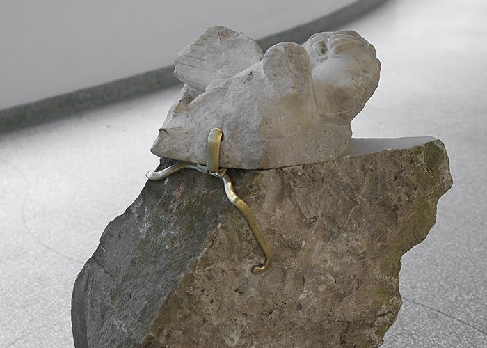 Close up detail, broken sleeping angel statue attached to a rock with a gold clasp.