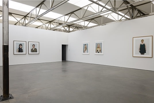 Installation image of various portraits in a white room.