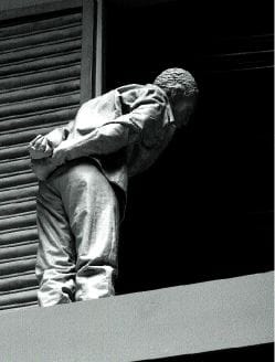 Metal statue of figure holding their hands behind their back peering down into blackness.