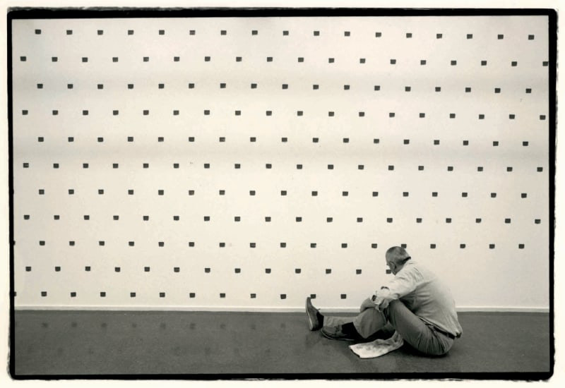 A sepia-toned image of Niele Toroni working on an installation