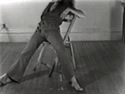 Black and white image of person from the shoulders down splayed on a chair, one leg leaning out of the frame.