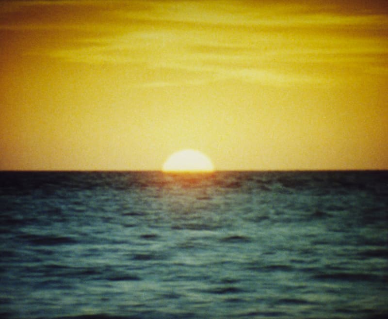 Grainy image of the sun setting above the ocean. 