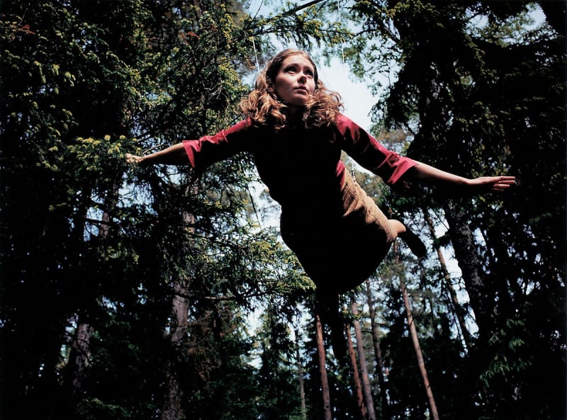 Person suspended by wires flies through a forest. 