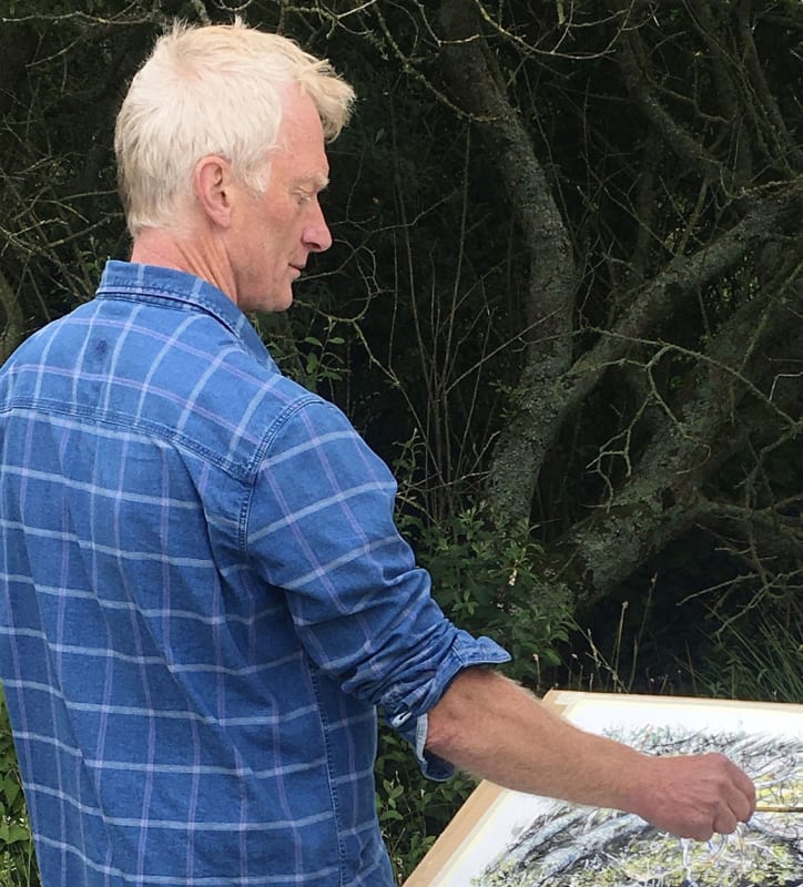 Nick Andrew artist profile photo painting outdoors, wearing a blue shirt
