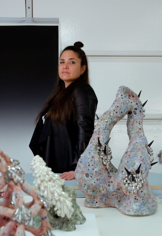 Sasha Koozel Reibstein posing for the camera next to her collection of abstract art sculptures.