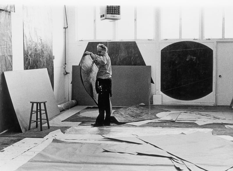 A black and white photograph of Manny Farber holding a large canvas preparing to paint his next contemporary masterpiece.