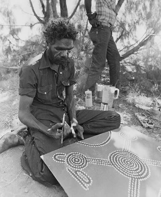 A black and white photo of Aboriginal-Australian artist Turkey Tolsen Tjupurrula painting an artwork, represented by Rebecca Hossack Art Gallery