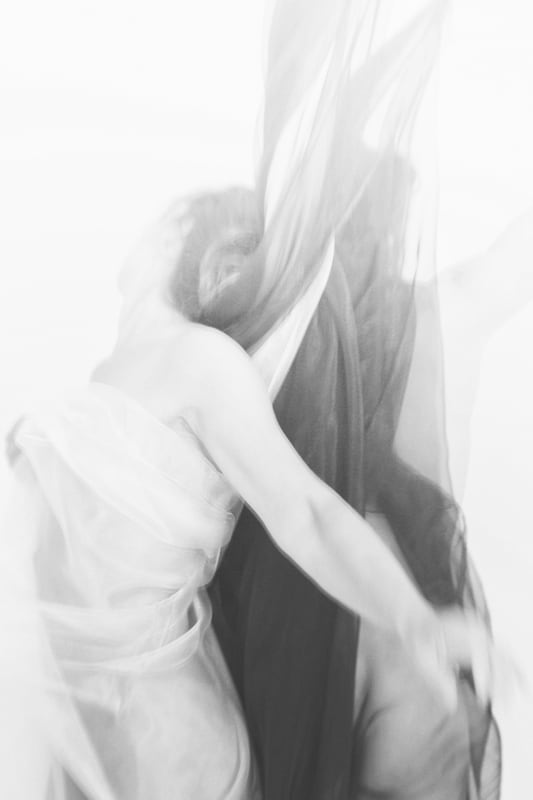 A black and white photo of a woman looking over her right shoulder loosely wrapped in flowing cloth by artist Margaret Lansink.