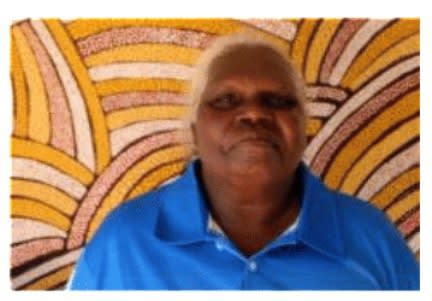 Paulina Puruntatameri in a blue top stood in front of an aboriginal artwork