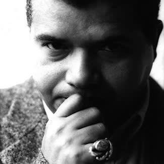 Black and white photograph of a man cropped to his head. He holds his chin in a thoughtful pose and looks directly at the camera.