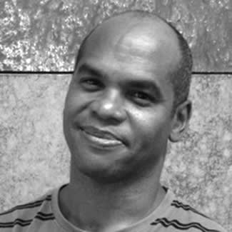 Black and white photograph of a lightly smiling man staring directly at the camera. He is slightly balding with close-cropped hair and no beard.