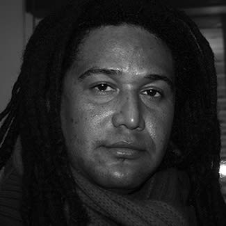 Black and white photograph of a dreadlocked man looked at the camera. x