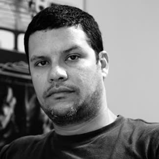 Black and white photograph of a man starting directly at the camera. He has a light beard under his chin and a light moustache. 